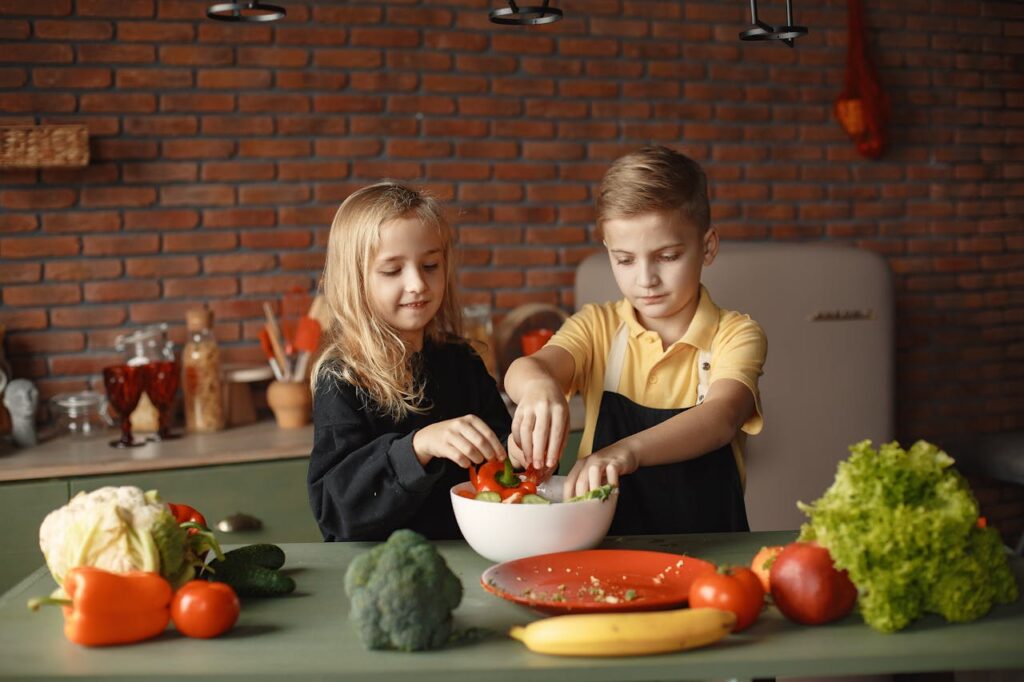 Little brother and sister washing fresh green vegetables together, learning healthy eating habits through everyday family activities.